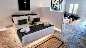 A modern bedroom with a stone floor, a bed with white and black bedding, and two abstract wall art pieces. - Mykonos Dot Art Homes - Premium Home One (Ano Mera)