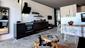 A modern living space with a kitchen, dining area, and a large window. - Mykonos Dot Art Homes - Premium Home One (Ano Mera)