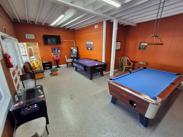 A pool table, a dartboard, a video game machine, and a billiards table in a room with orange walls and a ceiling with exposed beams. - Perfect full hookup 60ft campsite in Gatlinburg for your next adventure (Gatlinburg)