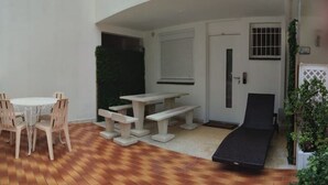 En terrasse med et rundt bord og stole, en bænk og en liggestol.