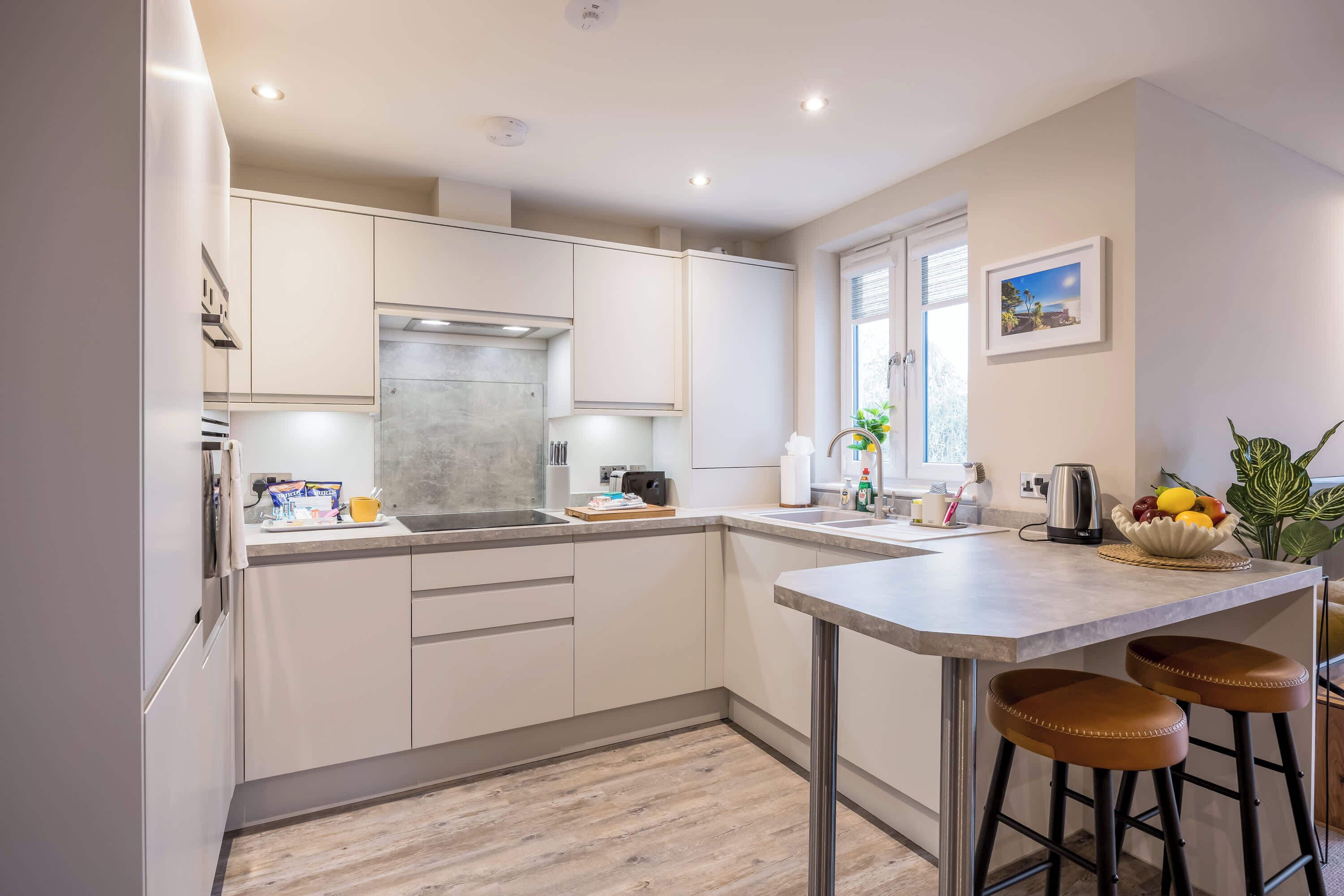 A modern kitchen with white cabinets, a stainless steel range hood, a sink, and a bar area with stools.