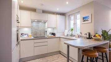 A modern kitchen with white cabinets, a stainless steel range hood, a sink, and a bar area with stools.
