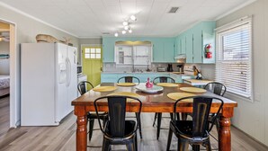 A dining area with a wooden table, black chairs, and a white refrigerator. - The Way Back: Cozy Cottage Steps to Beach + Hot Tub + Coffee with Private Suite (Kill Devil Hills)