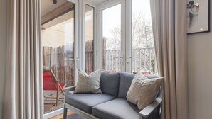 Una sala de estar moderna con un sofá gris, cortinas blancas y ventanas amplias.