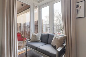 Ein modernes Wohnzimmer mit einem grauen Sofa, weißen Vorhängen und großen Fenstern.