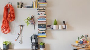 Una habitación con un escritorio de madera, una estantería llena de libros, un teléfono, una planta y una cafetera.