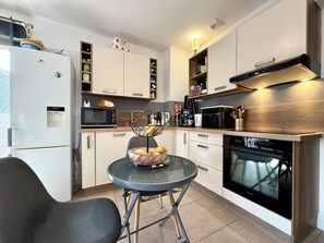 A compact kitchen with a refrigerator, microwave, oven, and a glass table with a bowl of fruit. - Propriano lovely 2-room apartment 46m2 with terrace&balcony (Propriano)