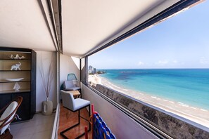 A balcony with a view of a beach and ocean. There is a chair, a small table, and a shelf with decorative items. - Isla Verde Oceanview 4BR With Private Beach Access (Carolina)
