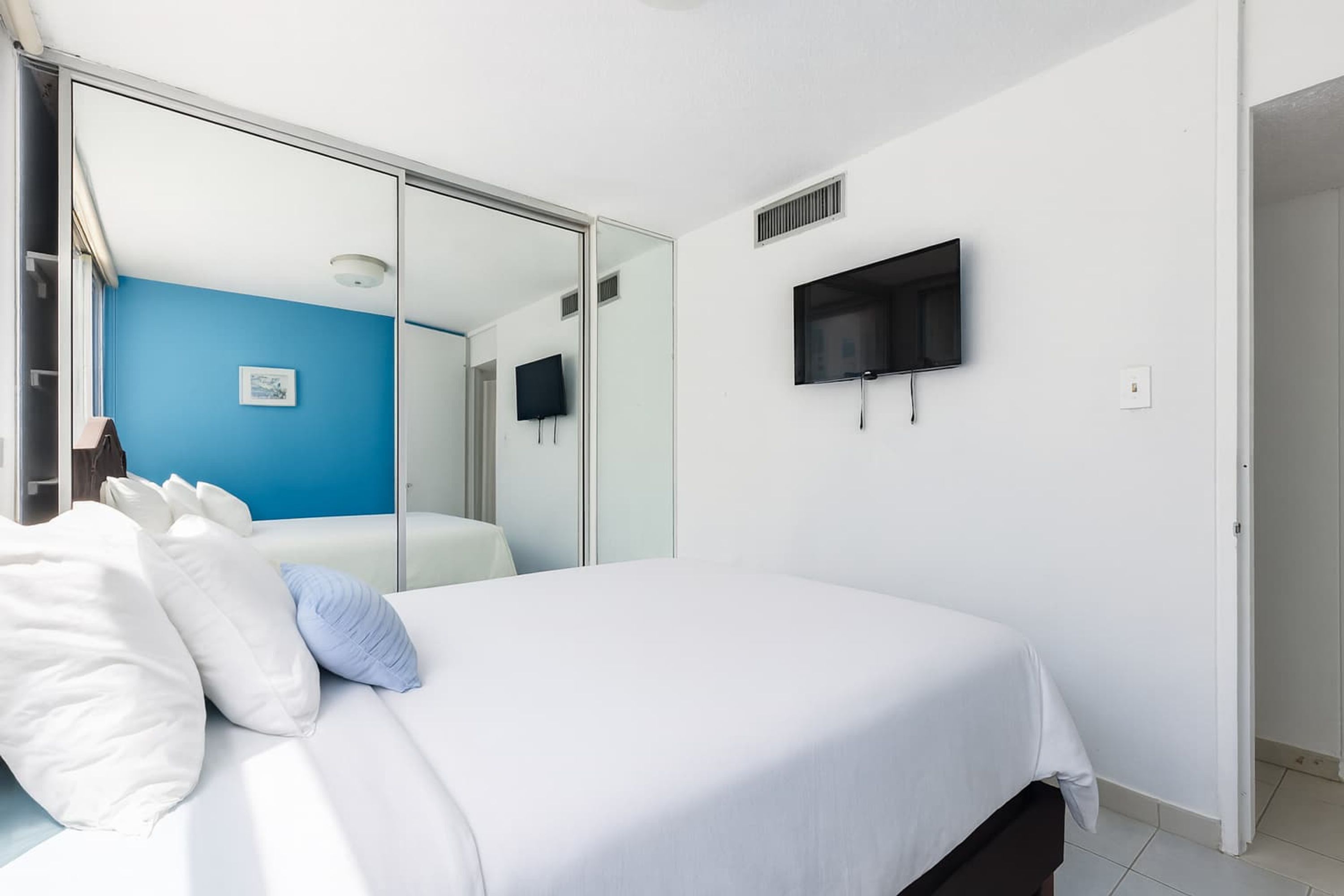 Un dormitorio con cama, televisor montado en la pared y puerta corrediza de vidrio que da al baño.