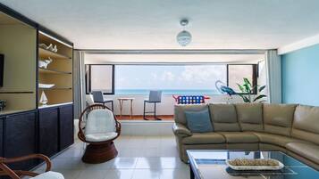 Un salón con sofá, sillas, mesa de centro y vista al mar.