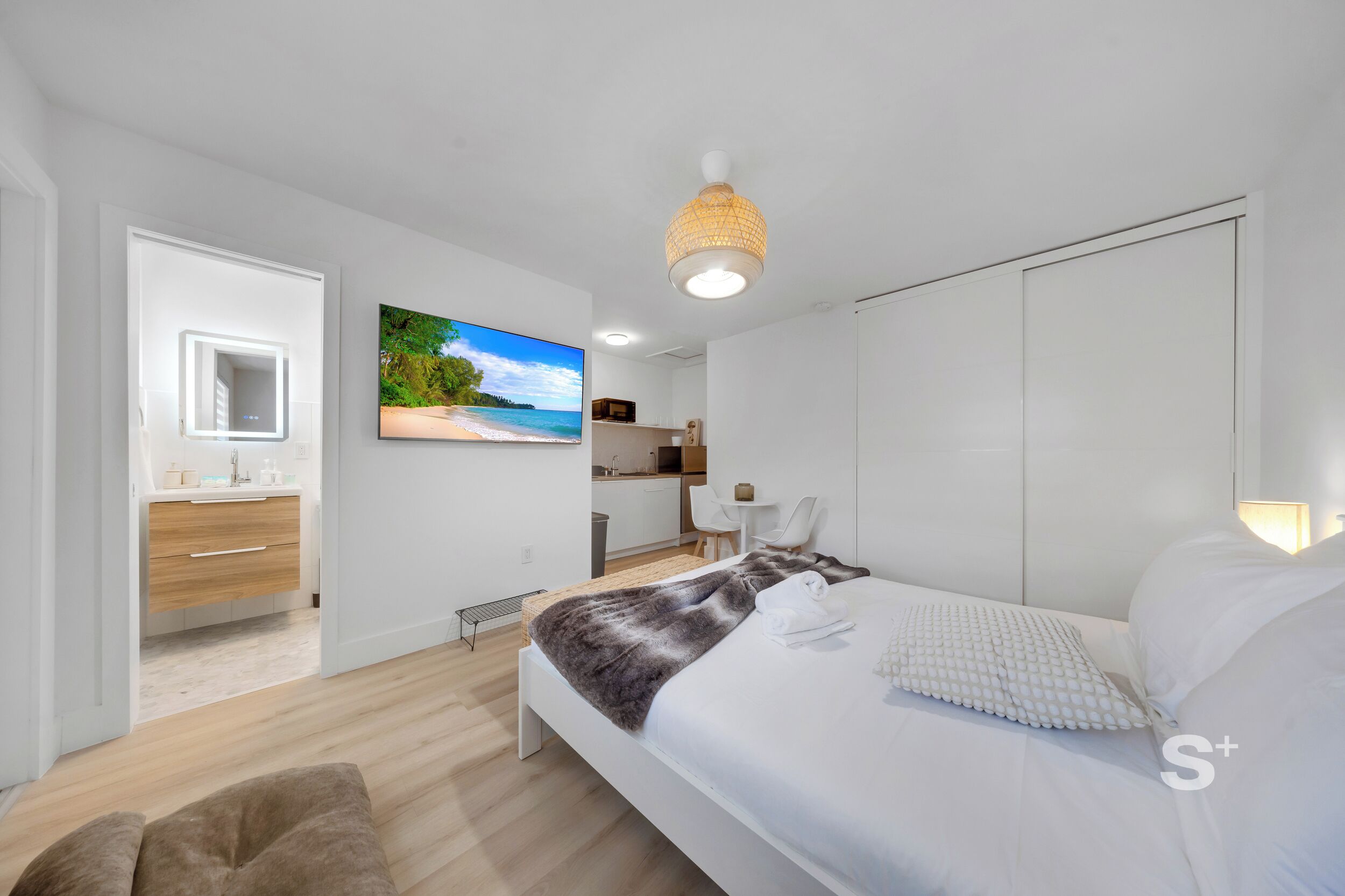 A modern bedroom with a bed, a TV, a bathroom, and a kitchen area.