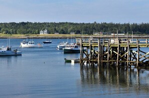 A marina with boats docked at wooden piers, surrounded by a forested shoreline. - Prospect Harbor Coastal Cottage | On the Water (Gouldsboro)
