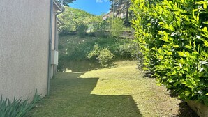 A grassy yard with a house on the left and a dense green bush on the right. - Le soleil d'eau 3 villa with terrace, parking (Meyras)