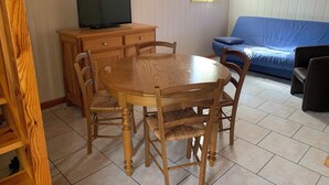 A dining area with a wooden table and chairs, a television on a wooden cabinet, and a blue sofa in the background. - Le soleil d'eau 3 villa with terrace, parking (Meyras)