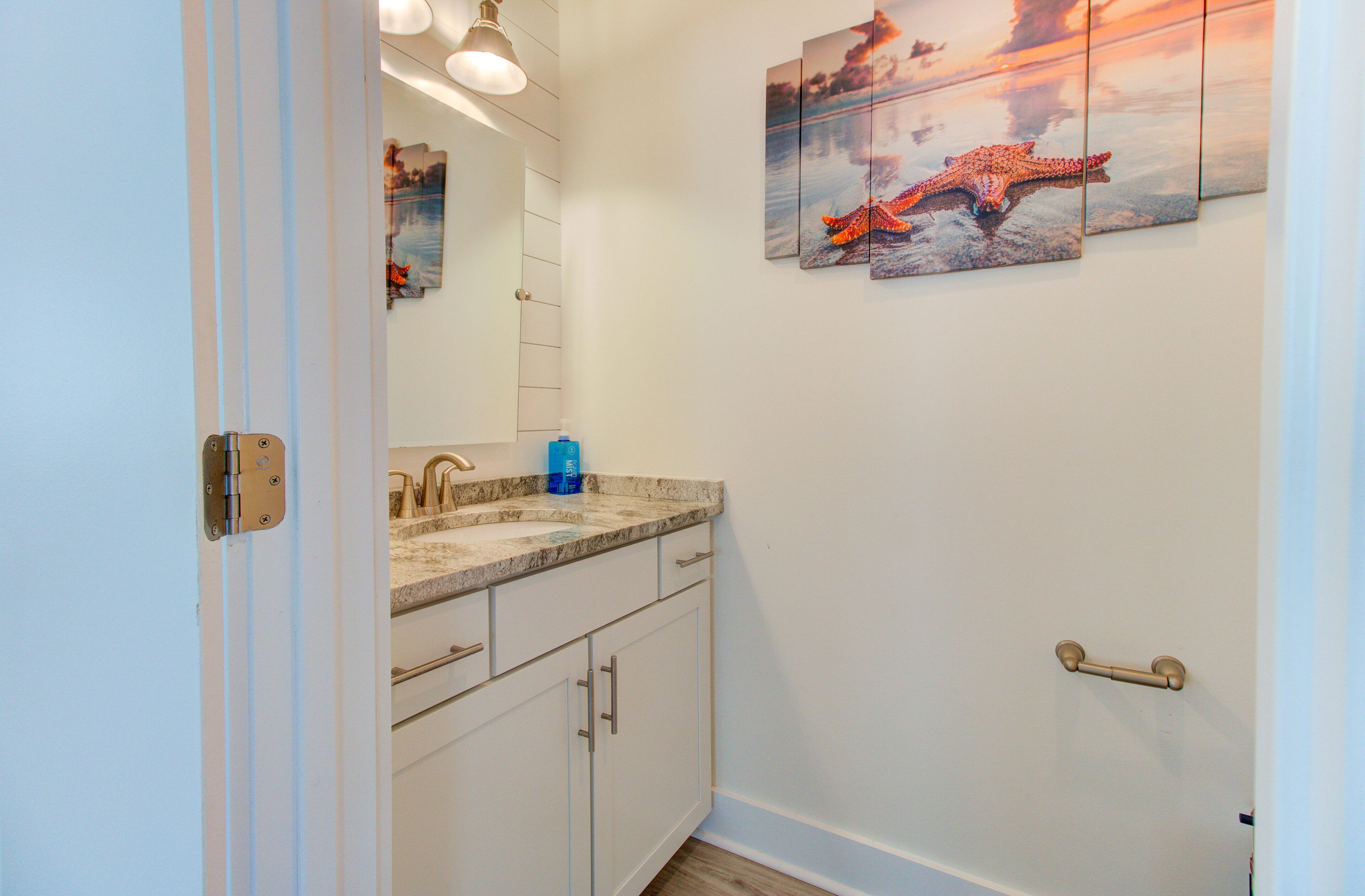 Une salle de bain avec un comptoir blanc, un lavabo et un miroir. Trois tableaux encadrés sont accrochés au mur.