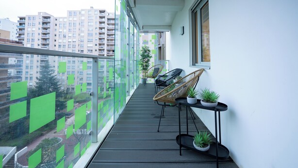 Ein Balkon mit Korbstühlen, Topfpflanzen und Blick auf eine Stadtlandschaft.