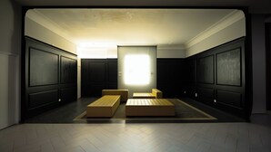 Ein Zimmer mit großem Fenster, dunklen Holzpaneelen und zwei beigefarbenen Poufs.
