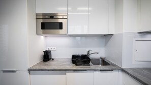 Una cocina moderna con armarios blancos, un horno de acero inoxidable, una cafetera y un lavamanos.