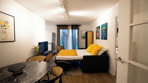 Ein kleines Hotelzimmer mit einem Bett, einem Schreibtisch, einem Stuhl, einem kleinen Tisch und einem Fernseher.