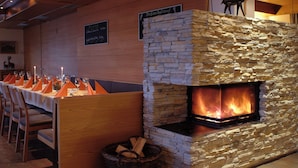 A restaurant with a stone fireplace, wooden tables, and chairs. - Landhotel Hoftaverne Atzmüller (Oberneukirchen)