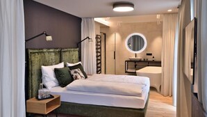 A modern bedroom with a green upholstered headboard, a round mirror above the vanity, and a neatly made bed with white linens. - Landhotel Hoftaverne Atzmüller (Oberneukirchen)