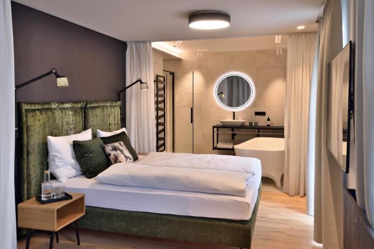 A modern bedroom with a green upholstered headboard, a round mirror above the vanity, and a neatly made bed with white linens.