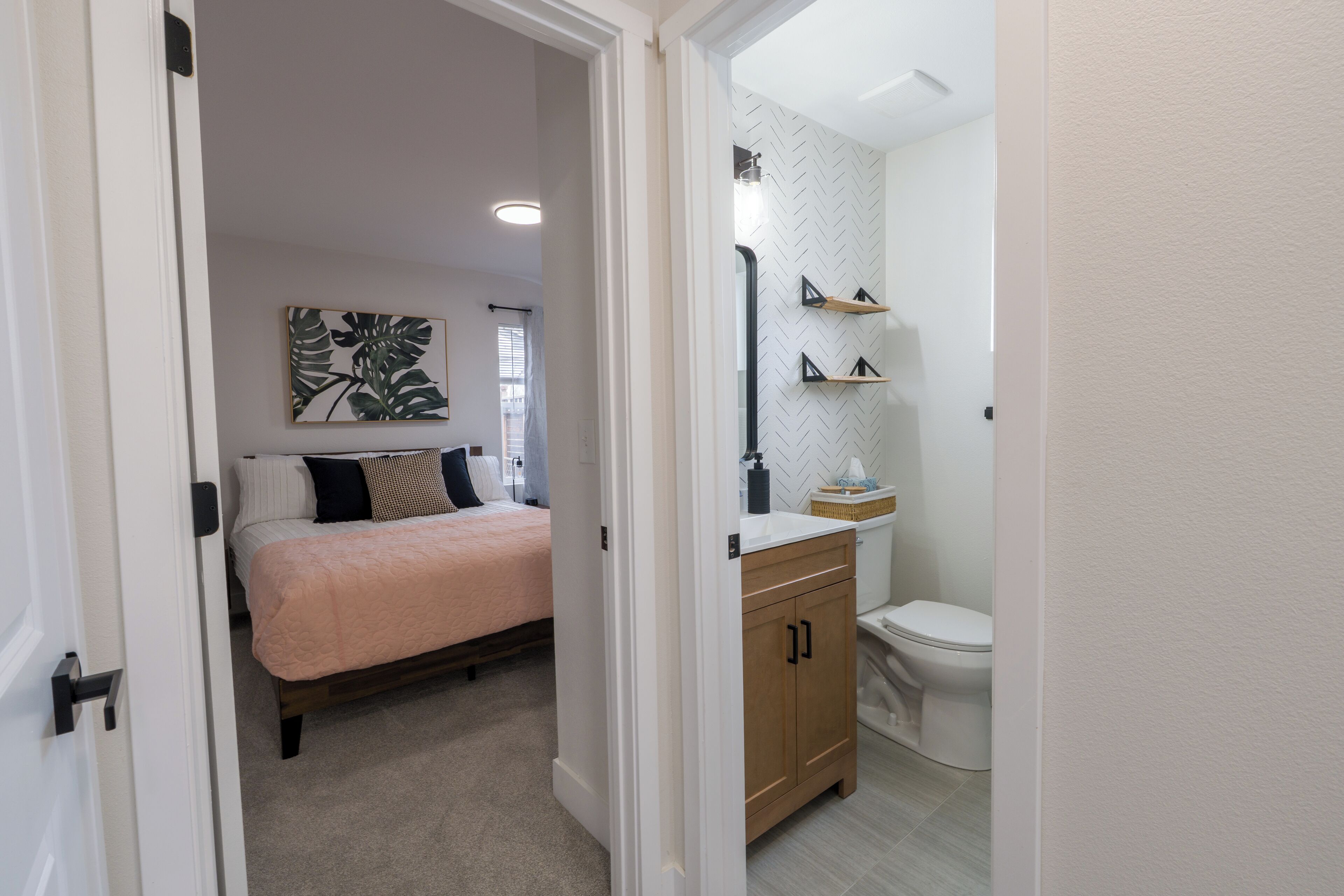 Un dormitorio con cama, mesita de noche y tocador. Cuenta con un baño con inodoro, lavamanos y espejo.