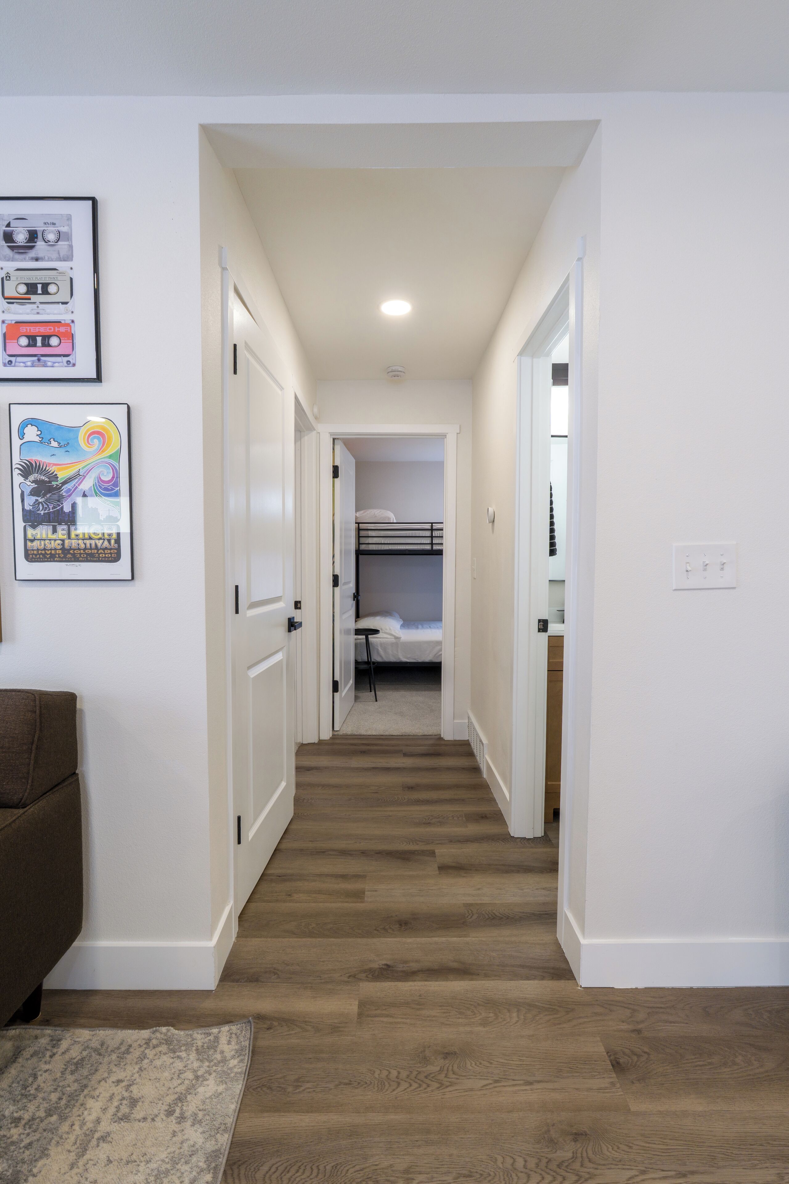 A narrow hallway with wooden flooring, white walls, and a bunk bed in the distance.