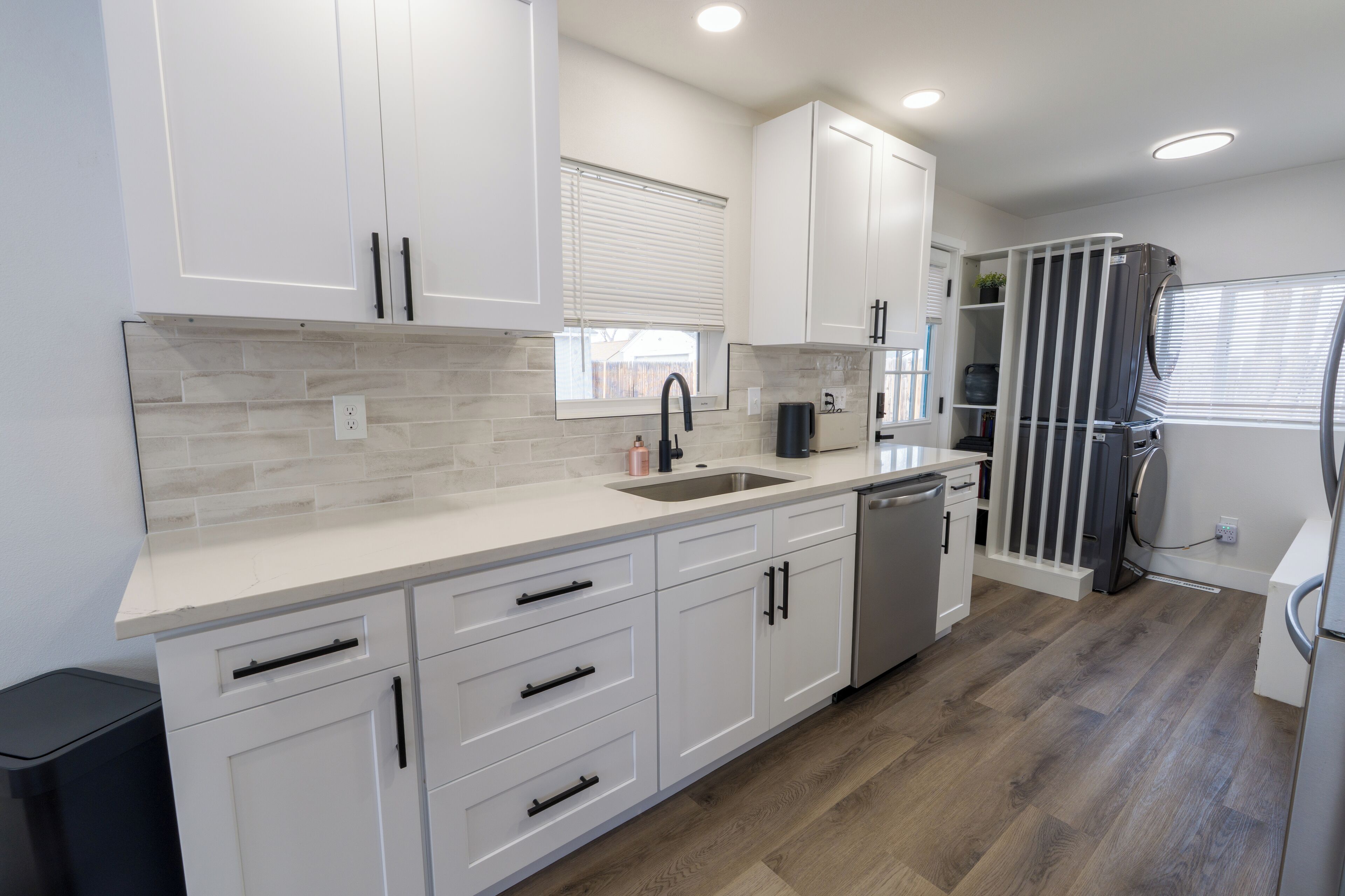 A modern kitchen with white cabinetry, a stainless steel sink, and a built-in dishwasher.