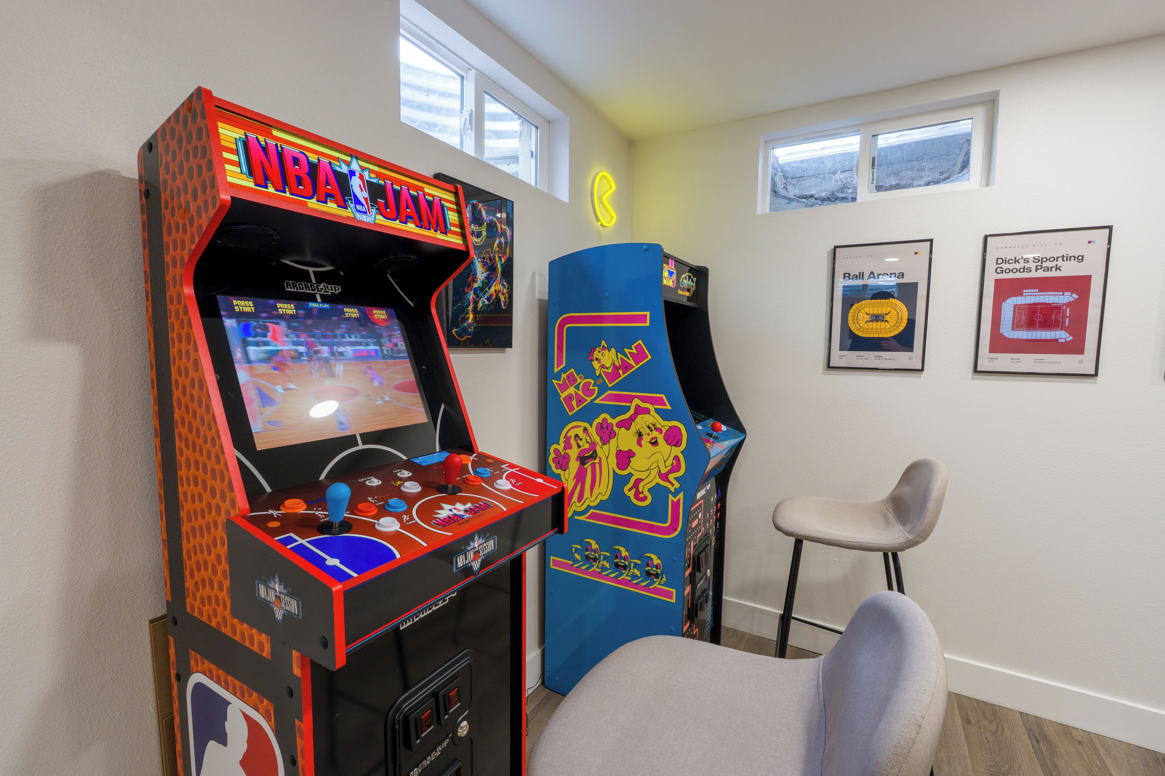 Une pièce avec deux bornes d’arcade, un panneau néon et deux tableaux encadrés accrochés au mur.