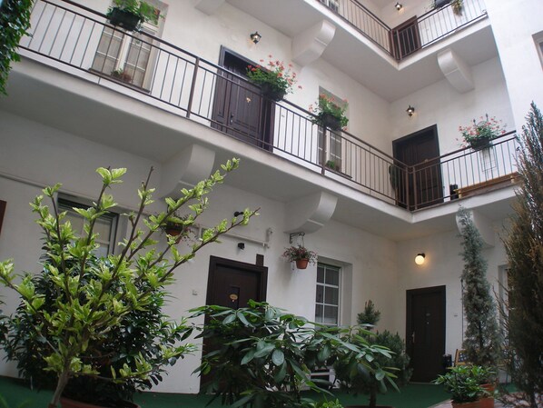 A multi-story building with balconies, potted plants, and a green carpeted area. - Aparthotel Davids (Prague)