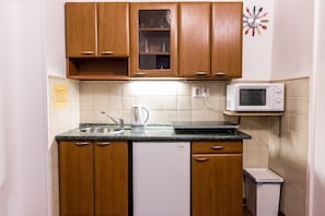 A compact kitchen with wooden cabinets, a microwave, a kettle, and a small refrigerator. - Aparthotel Davids (Prague)