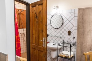A bathroom with a wooden door, a white sink, a mirror, and a towel rack with towels. - Aparthotel Davids (Prague)