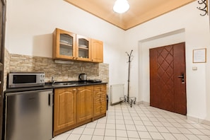 A compact kitchen with a microwave, stove, wooden cabinets, and a tiled floor. - Aparthotel Davids (Prague)