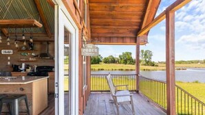 En veranda av trä med en skylt som visar texten ”The Porch”, ett barområde med barstolar och utsikt över en sjö.