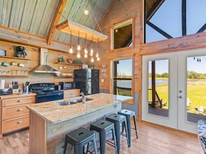 A spacious kitchen with a large island, bar stools, and a view of the outdoors. - Rustic Cabin Retreat with Fishing, Hiking & Outdoor Adventures (Bullock County)