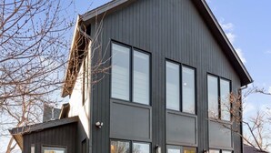 Ein modernes, zweistöckiges Haus mit dunkler Fassade, großen Fenstern und einer Veranda mit Treppe.