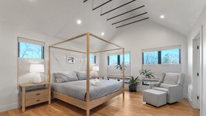Ein modernes Schlafzimmer mit einem Himmelbett, Nachttischen, einem Sessel und einem Blumentopf.