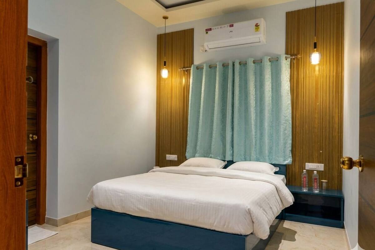 Um quarto com uma cama, um guarda-roupa de madeira, um banco azul e um aparelho de ar condicionado.
