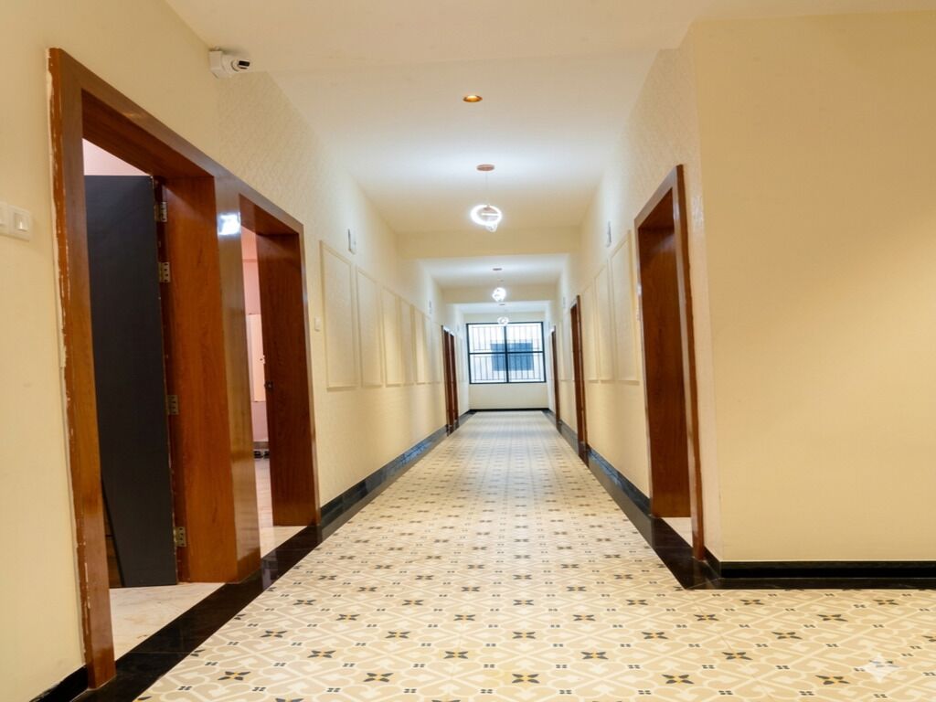 A long, narrow hallway with patterned flooring, wooden doors, and a ceiling light.