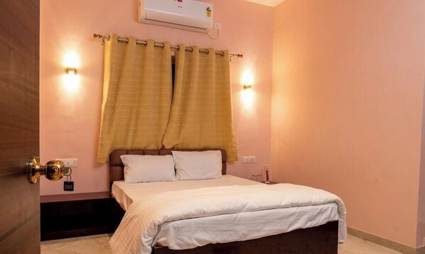 A bedroom with a bed, curtains, wall-mounted lights, an air conditioner, and a door with a lock. - Raj Royal Hotel (Nagpur)