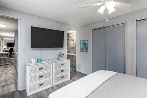 Ein Schlafzimmer mit einem Bett, einer Kommode mit Schubladen, einem Flachbildfernseher und einem Deckenventilator.