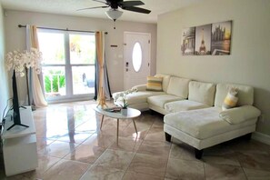 A living room with a white sofa, a coffee table, and a flat-screen TV. - Family Oasis with Pool and Spa (Tampa)