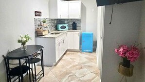 Eine kleine Küche mit weißen Schränken, einem blauen Kühlschrank und einem Essbereich mit einem schwarzen Tisch und Stühlen.