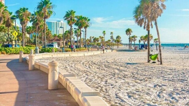 Ein Strand mit Palmen, einem Sandweg und einem Gebäude im Hintergrund.