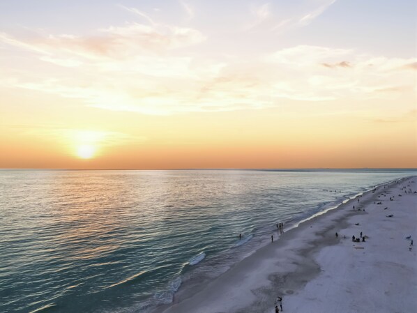 Ein Strand bei Sonnenuntergang, ruhiges Meer und Menschen am Ufer.