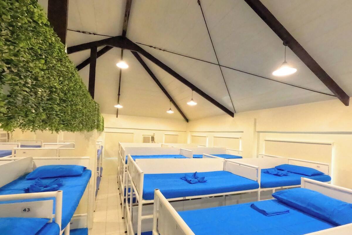 Une chambre d’hôpital avec plusieurs lits, chacun doté d’un matelas bleu et d’une tête de lit blanche.