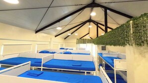 A dormitory-style room with bunk beds, a high ceiling with exposed beams, and a green wall decoration. - The Luneta Seafarers Center Premier Dorm (Manila)