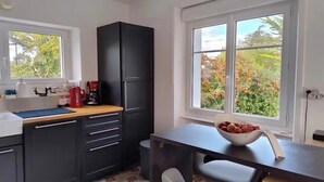 Una cocina compacta con armarios oscuros, una cafetera y un bol de fruta en la encimera.