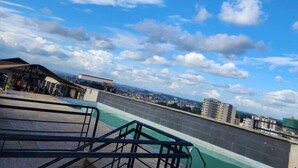 Ein Pool auf dem Dach mit Blick auf die Stadt, Metallgeländern und wolkenlosem Himmel.